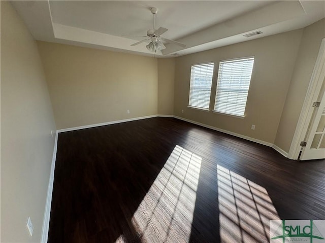 empty room with dark hardwood / wood-style floors, a raised ceiling, and ceiling fan