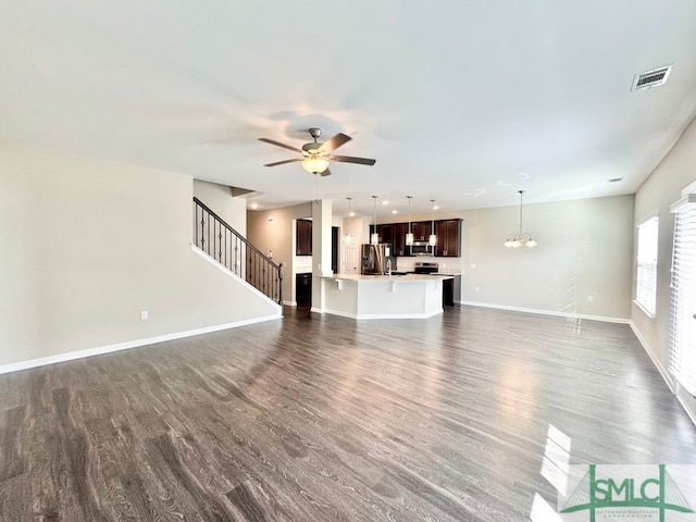 unfurnished living room with visible vents, baseboards, dark wood finished floors, stairs, and ceiling fan with notable chandelier