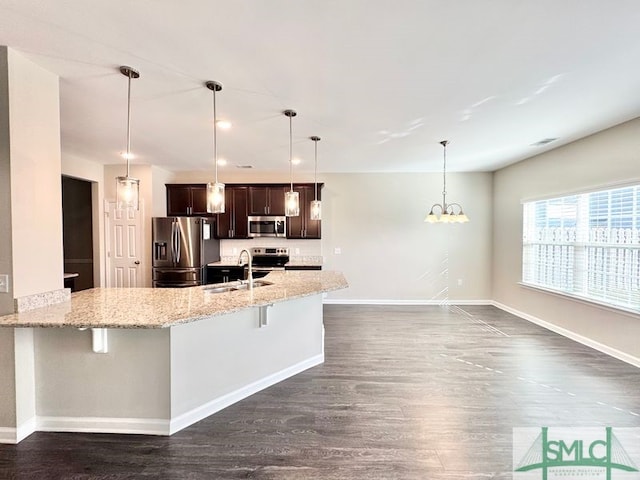 kitchen with a sink, light stone counters, stainless steel appliances, a breakfast bar area, and dark brown cabinets