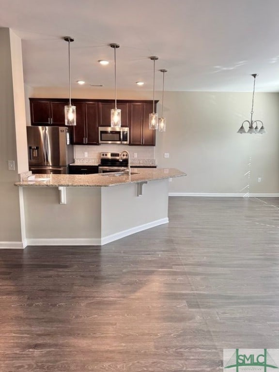 kitchen with dark brown cabinetry, stainless steel appliances, a kitchen bar, and baseboards