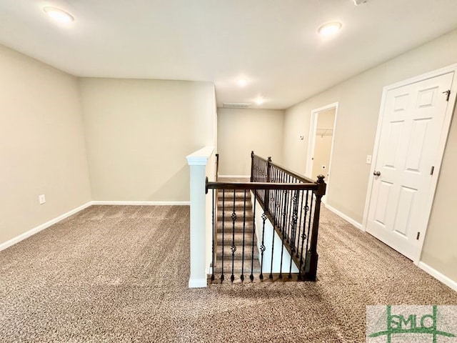 hallway with an upstairs landing, baseboards, and carpet