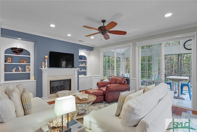 living room featuring built in shelves, ceiling fan, ornamental molding, and hardwood / wood-style flooring