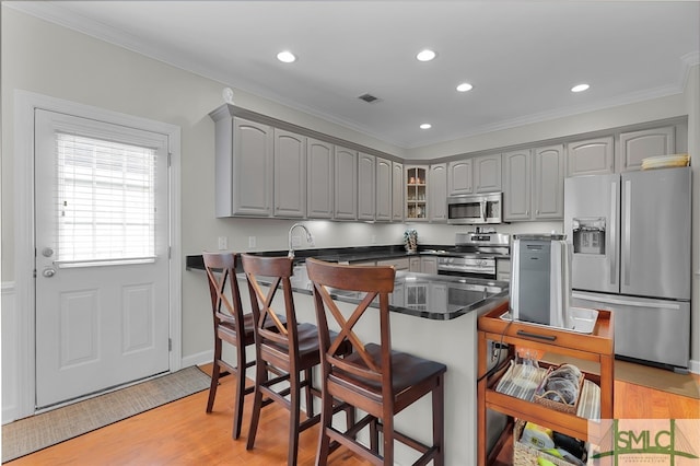 kitchen featuring gray cabinetry, light hardwood / wood-style floors, a kitchen bar, kitchen peninsula, and stainless steel appliances