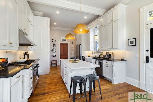 kitchen with decorative light fixtures, a center island, white cabinetry, appliances with stainless steel finishes, and a breakfast bar area