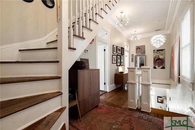 stairs with plenty of natural light, hardwood / wood-style floors, crown molding, and a chandelier