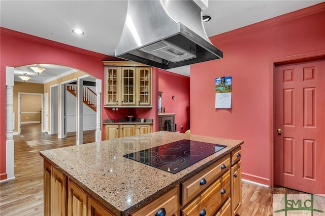 kitchen featuring black electric stovetop, light wood-type flooring, crown molding, a kitchen island, and range hood