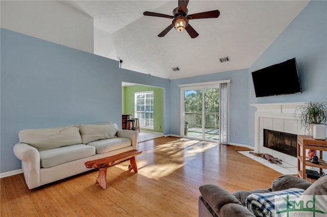 living room with a tile fireplace, ceiling fan, high vaulted ceiling, and light wood-type flooring