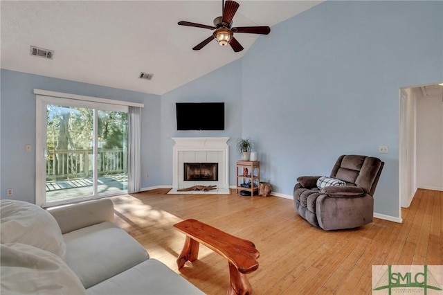 living room with ceiling fan, light hardwood / wood-style floors, high vaulted ceiling, and a tiled fireplace