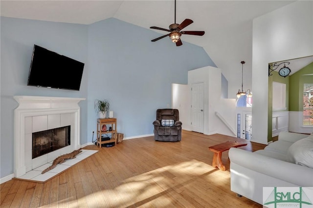 living room featuring a tiled fireplace, high vaulted ceiling, wood-type flooring, and ceiling fan with notable chandelier