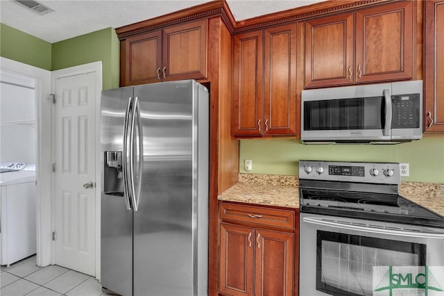 kitchen with stainless steel appliances, light stone counters, a textured ceiling, light tile patterned floors, and washer and dryer