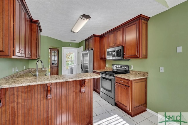 kitchen featuring sink, a textured ceiling, light tile patterned flooring, kitchen peninsula, and stainless steel appliances