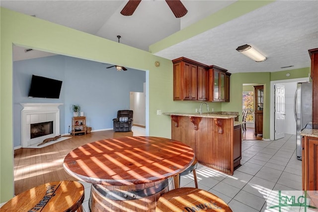 kitchen with a tile fireplace, a kitchen breakfast bar, kitchen peninsula, stainless steel fridge, and light wood-type flooring