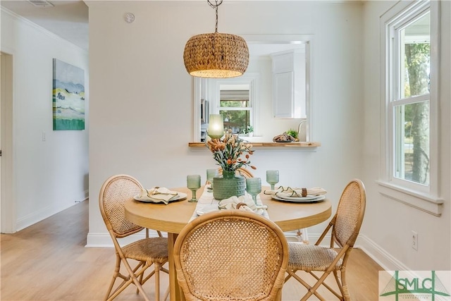 dining space with a wealth of natural light, crown molding, and light hardwood / wood-style floors