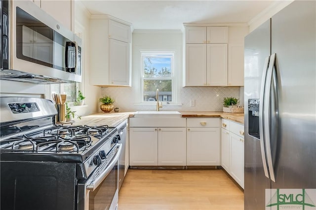 kitchen with stainless steel appliances, light wood-type flooring, crown molding, white cabinets, and sink