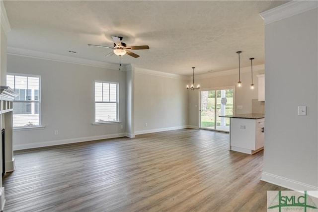 unfurnished living room featuring ceiling fan with notable chandelier, crown molding, light wood-type flooring, and a fireplace