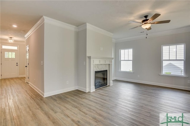 unfurnished living room featuring a premium fireplace, ceiling fan, light hardwood / wood-style floors, and ornamental molding