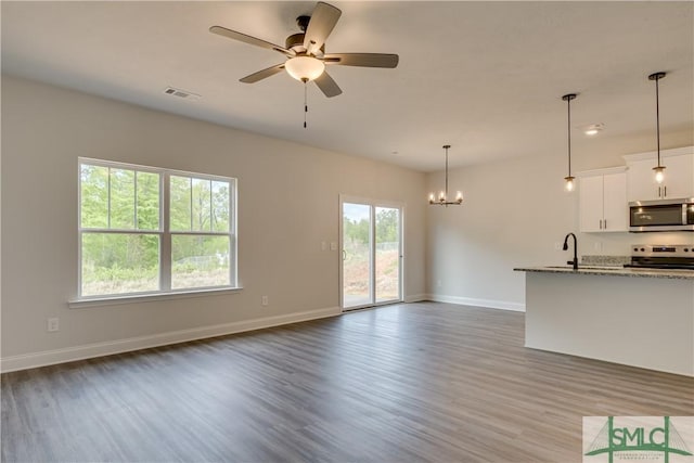 unfurnished living room featuring dark hardwood / wood-style floors, sink, ceiling fan with notable chandelier, and a wealth of natural light