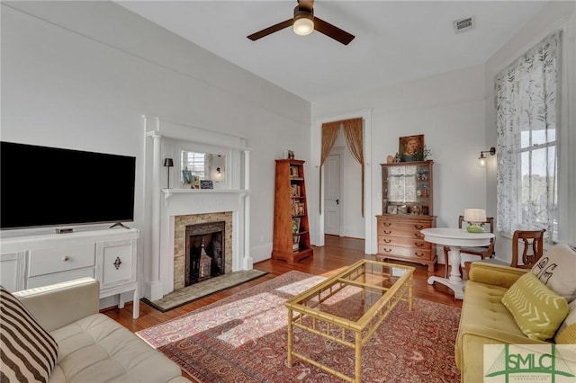 living room with ceiling fan, light hardwood / wood-style floors, and a stone fireplace