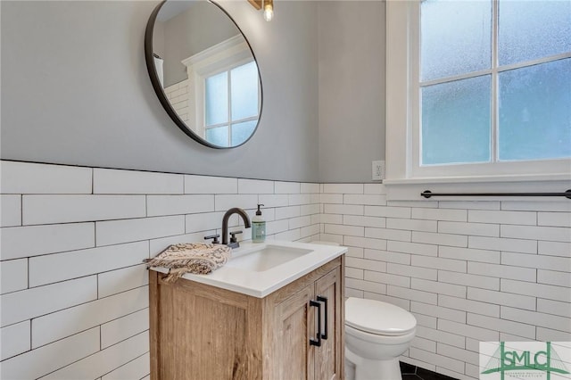 bathroom with a wealth of natural light, vanity, tile walls, and toilet