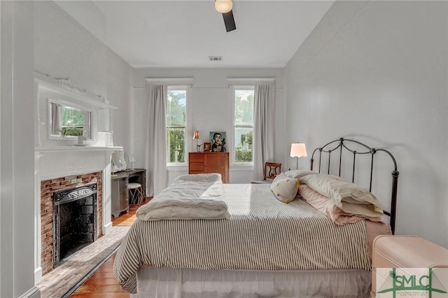 bedroom featuring hardwood / wood-style flooring, a brick fireplace, and ceiling fan