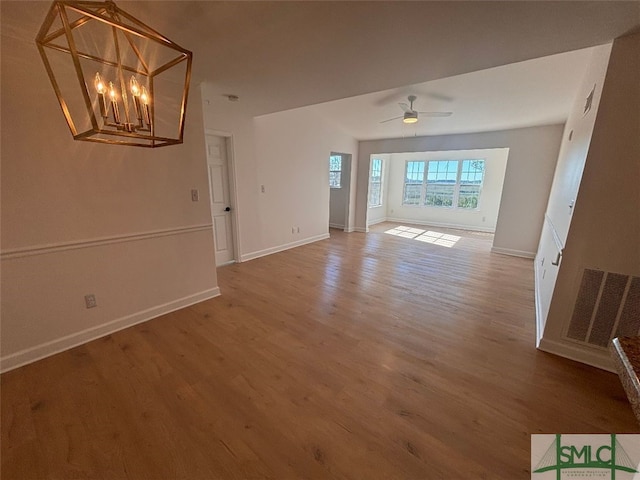 unfurnished living room featuring ceiling fan with notable chandelier and wood-type flooring