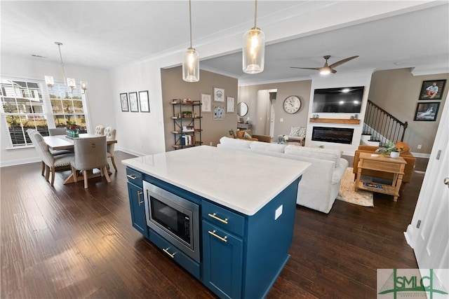 kitchen featuring ceiling fan with notable chandelier, blue cabinets, dark wood-type flooring, pendant lighting, and stainless steel microwave