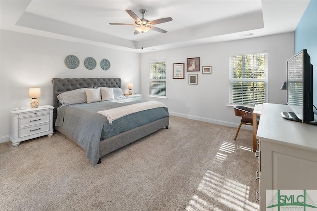 carpeted bedroom with a raised ceiling and ceiling fan