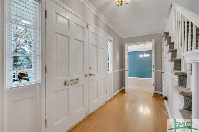 foyer with an inviting chandelier, ornamental molding, and light hardwood / wood-style flooring