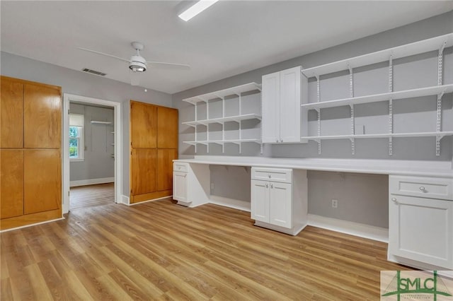 unfurnished office featuring ceiling fan, built in desk, and light hardwood / wood-style flooring