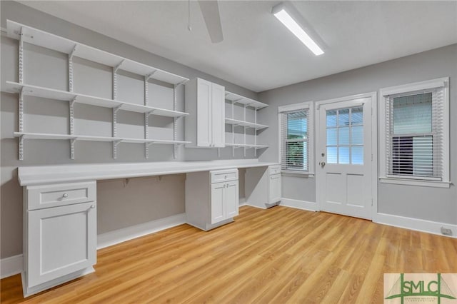 unfurnished office featuring ceiling fan, built in desk, and light wood-type flooring