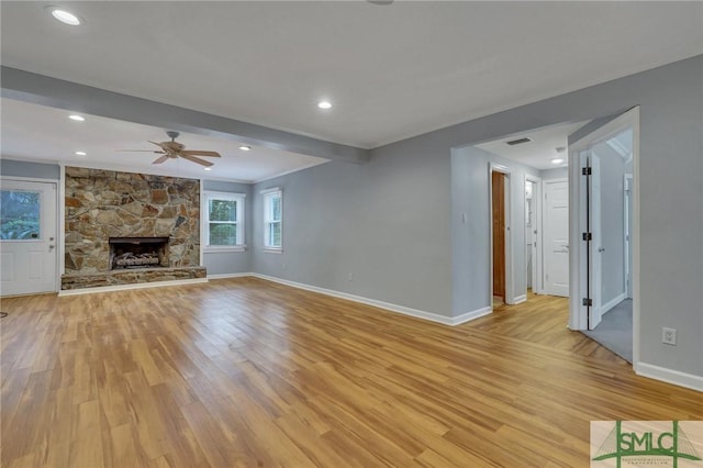 unfurnished living room featuring ceiling fan, light hardwood / wood-style floors, and a stone fireplace