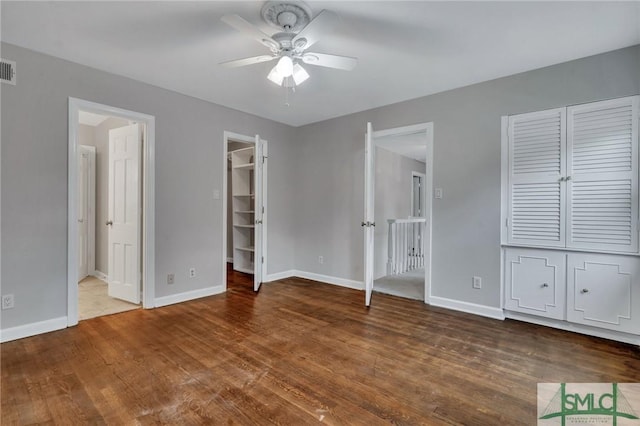 unfurnished bedroom featuring ceiling fan, wood-type flooring, a walk in closet, and ensuite bath