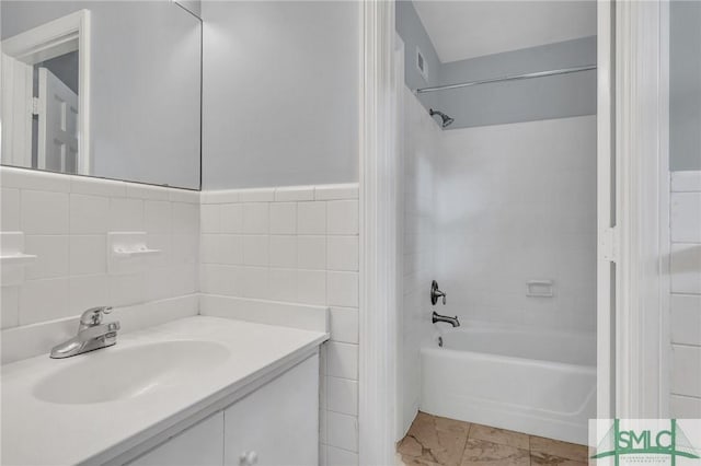 bathroom with tiled shower / bath, vanity, and tile walls