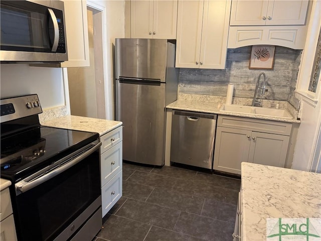 kitchen with light stone countertops, backsplash, stainless steel appliances, sink, and dark tile patterned flooring