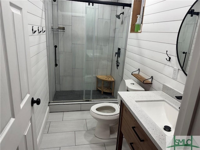 bathroom featuring tile patterned floors, vanity, toilet, a shower with shower door, and wood walls