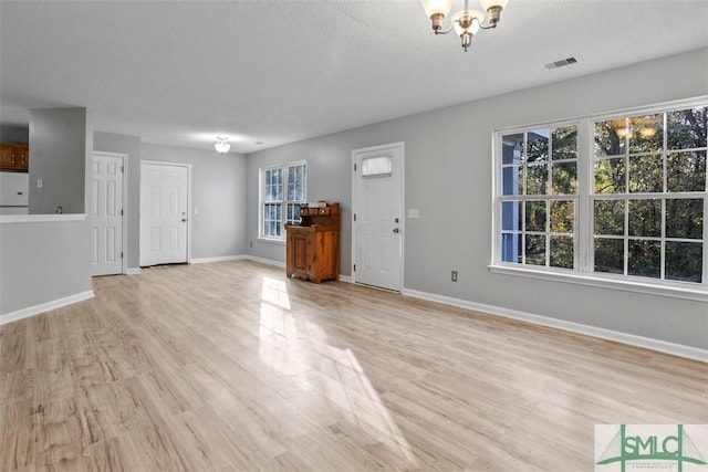 unfurnished living room featuring a notable chandelier, light wood-type flooring, and a textured ceiling