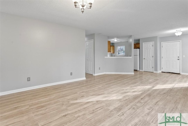 unfurnished living room featuring light wood-type flooring, a textured ceiling, and a chandelier