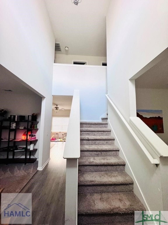 stairs featuring ceiling fan, wood-type flooring, and a high ceiling