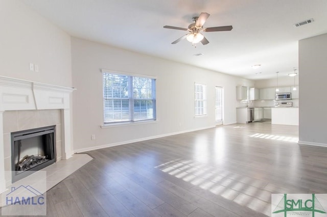 unfurnished living room with hardwood / wood-style flooring, a tile fireplace, and ceiling fan