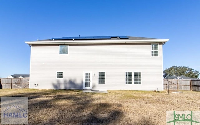 rear view of property featuring a yard and solar panels