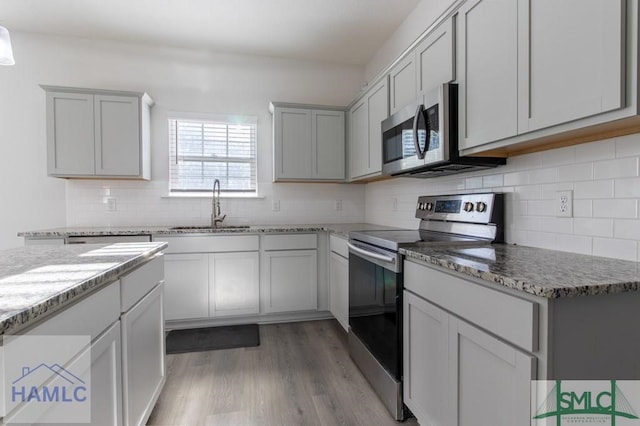 kitchen with sink, stainless steel appliances, light stone counters, and light hardwood / wood-style flooring