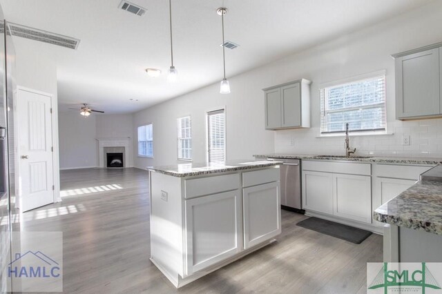 kitchen with a center island, gray cabinetry, stainless steel dishwasher, sink, and decorative light fixtures