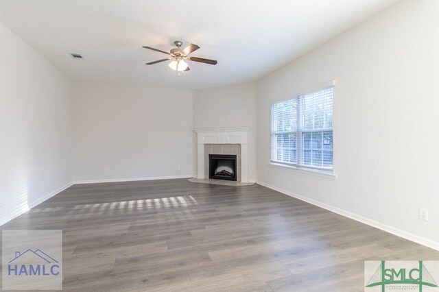 unfurnished living room with ceiling fan, wood-type flooring, and a tile fireplace