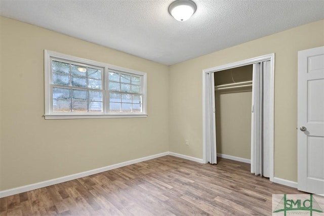 unfurnished bedroom with a textured ceiling, light wood-type flooring, and a closet