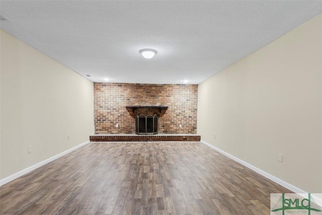 unfurnished living room with brick wall, wood-type flooring, a textured ceiling, and a brick fireplace