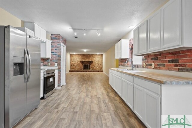 kitchen with white cabinets, sink, appliances with stainless steel finishes, butcher block counters, and brick wall