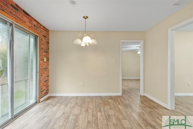 unfurnished room featuring brick wall, light hardwood / wood-style flooring, a healthy amount of sunlight, and a notable chandelier