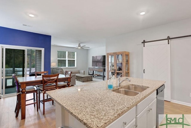 kitchen featuring a kitchen island with sink, sink, a barn door, light hardwood / wood-style floors, and white cabinetry