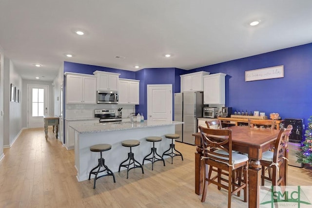 kitchen featuring a kitchen island with sink, light hardwood / wood-style floors, light stone counters, white cabinetry, and stainless steel appliances