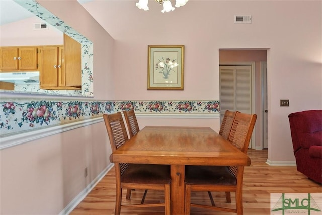 dining room with a chandelier, vaulted ceiling, and light wood-type flooring